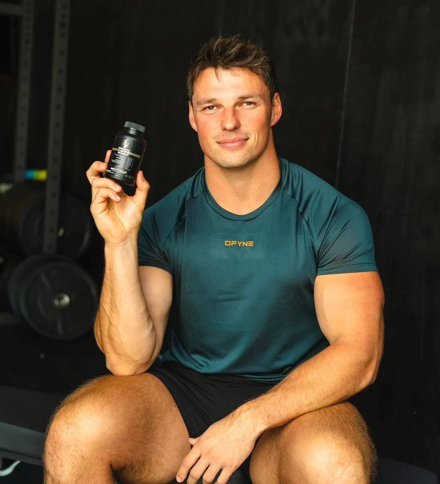 Steven holding the NattyPLUS Ultimate Testosterone Booster in the gym