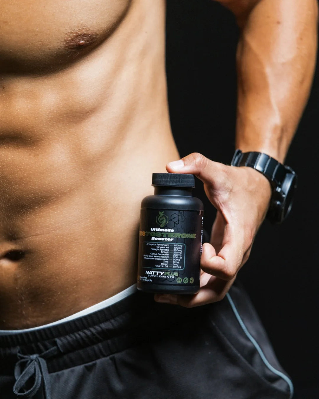 Gabe holding the Ultimate Testosterone Booster bottle against his torso, label facing out