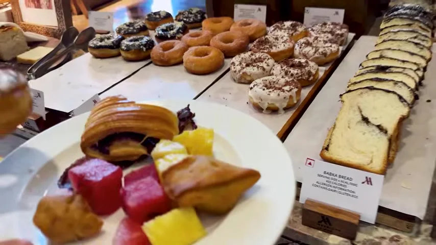 A hotel breakfast buffet of donuts, pastries and babka, with a loaded plate in the foreground