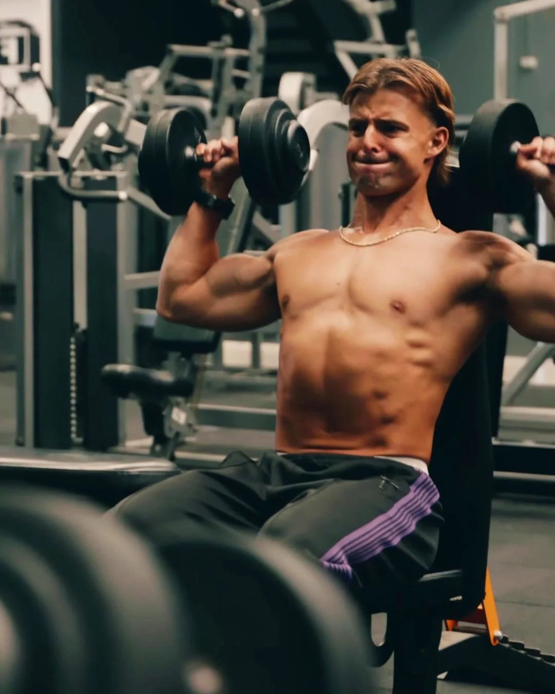 Gabe pressing dumbbells overhead in the gym