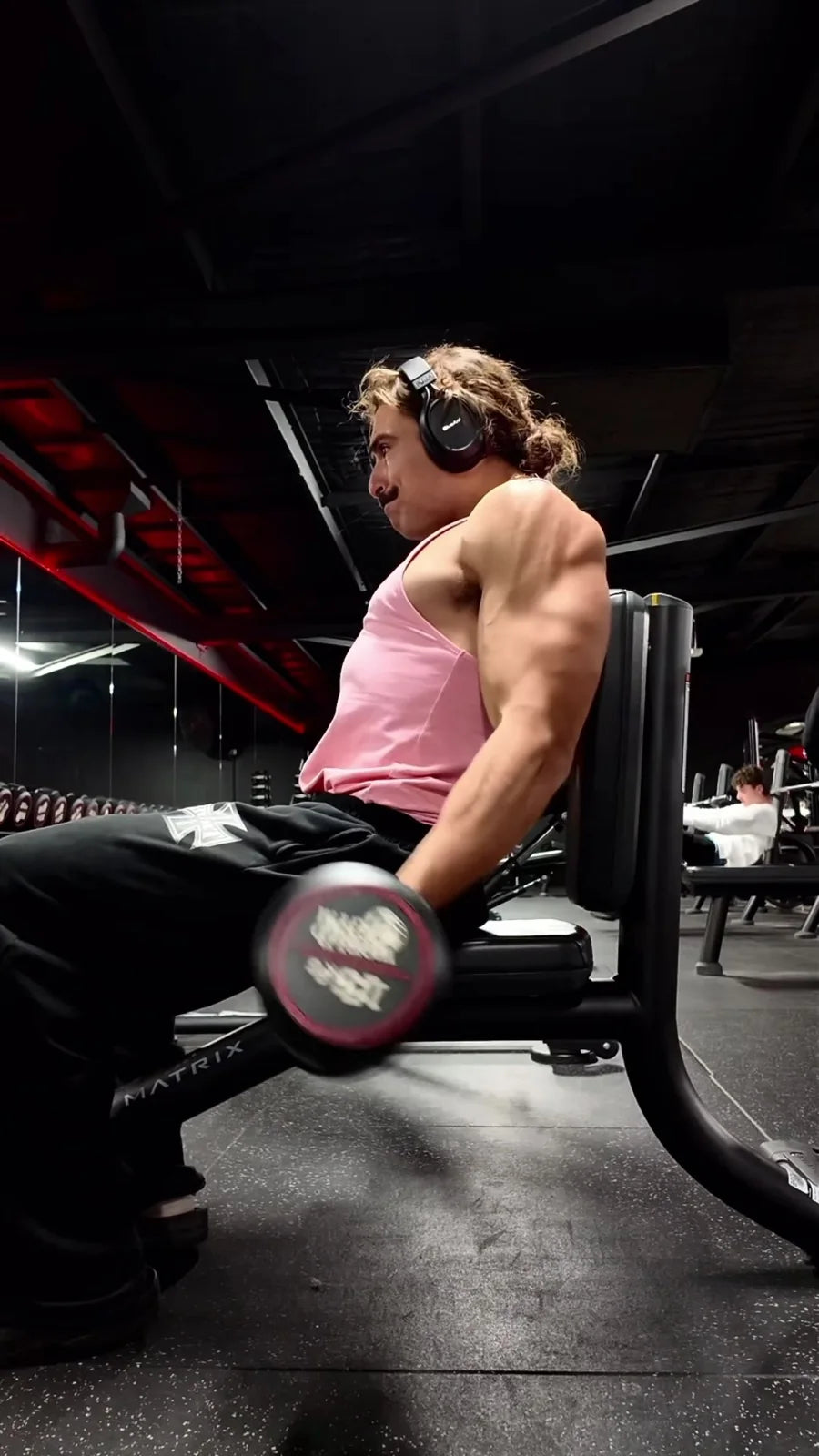 Rambo doing seated dumbbell curls in a pink singlet